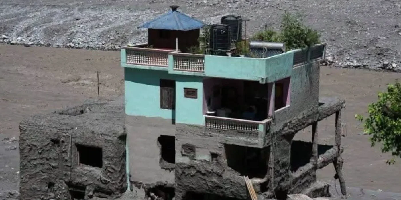 A house standing intact above a first floor packed solid with grey flood mud, surrounded by a flat plain of silt