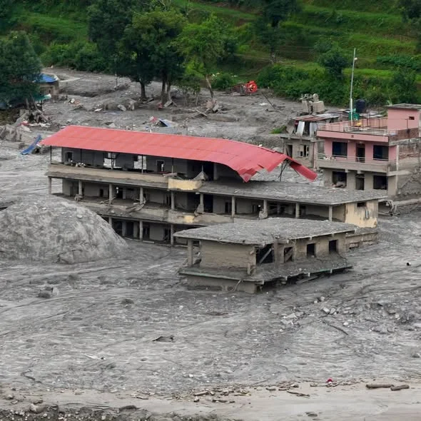 A large multi-storey building with a collapsed red roof, buried to its second floor in flood silt