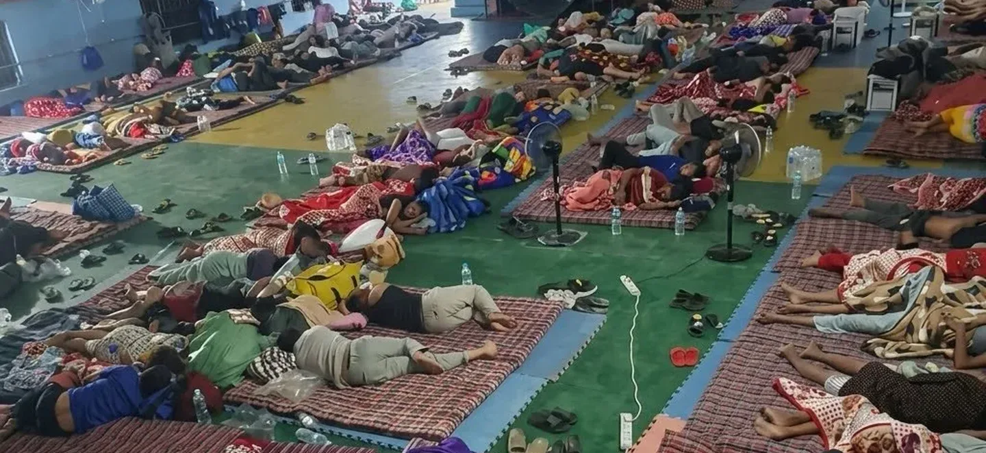Displaced families asleep on mats laid out in rows across the floor of a covered hall in Trishuli, Nuwakot
