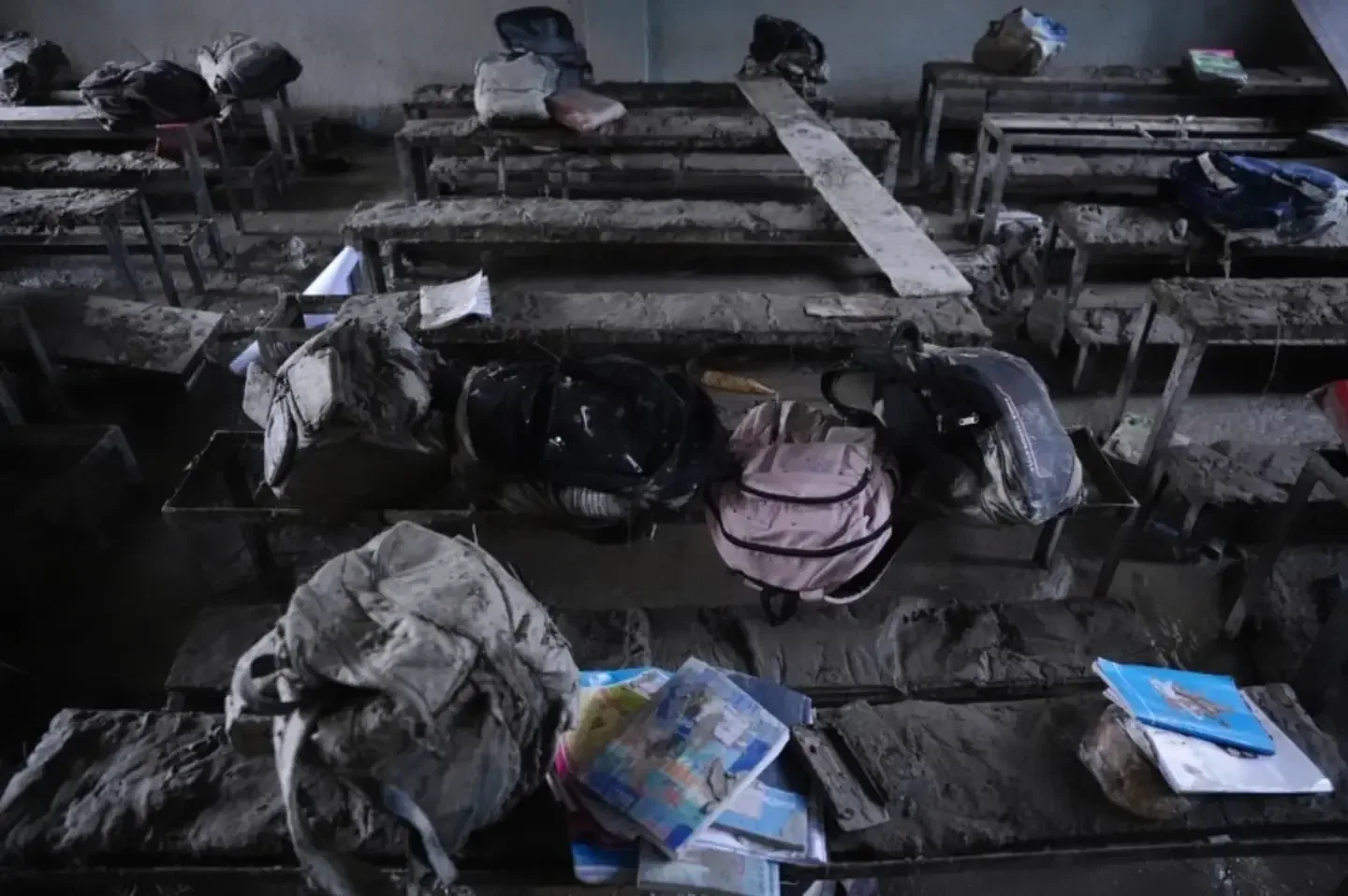 A classroom filled with dried grey silt, school bags and exercise books left on the benches