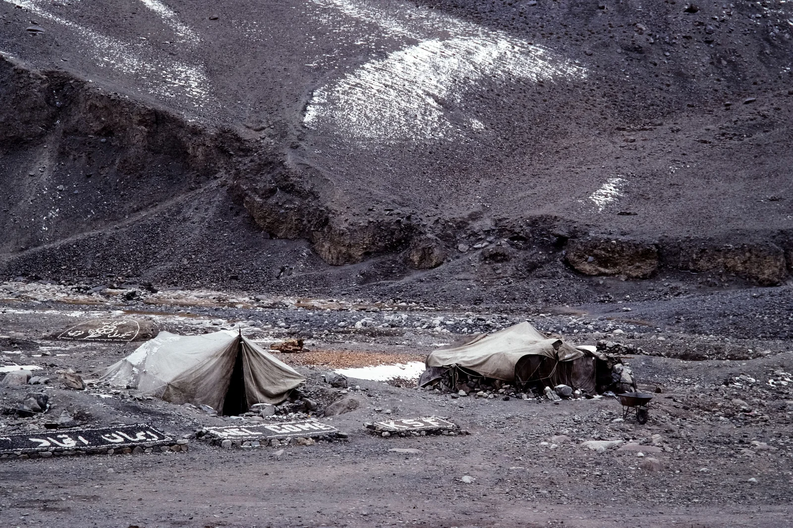 Canvas tents on rocky moraine below a mountainside