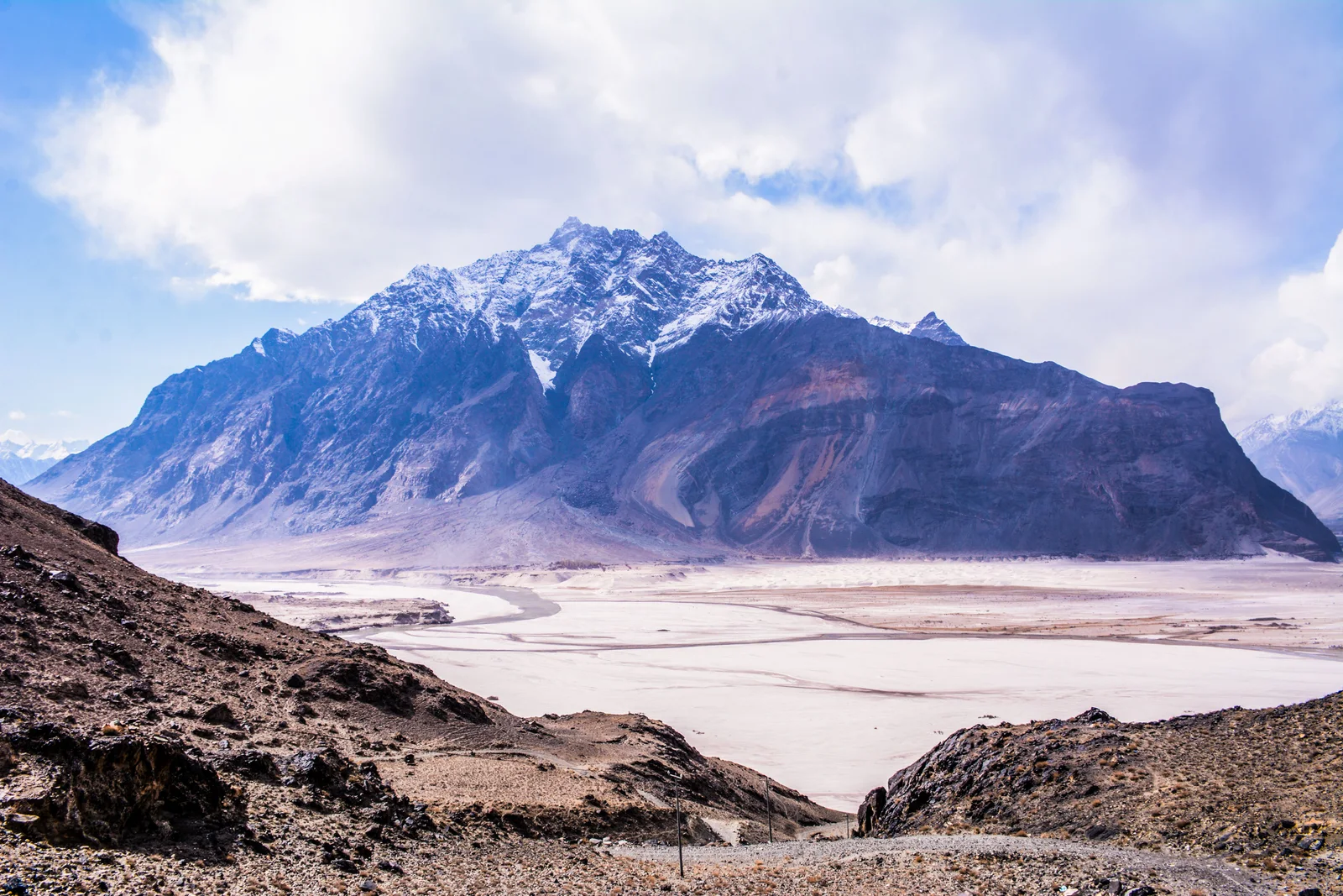 A snow-capped mountain above a wide, dry river valley