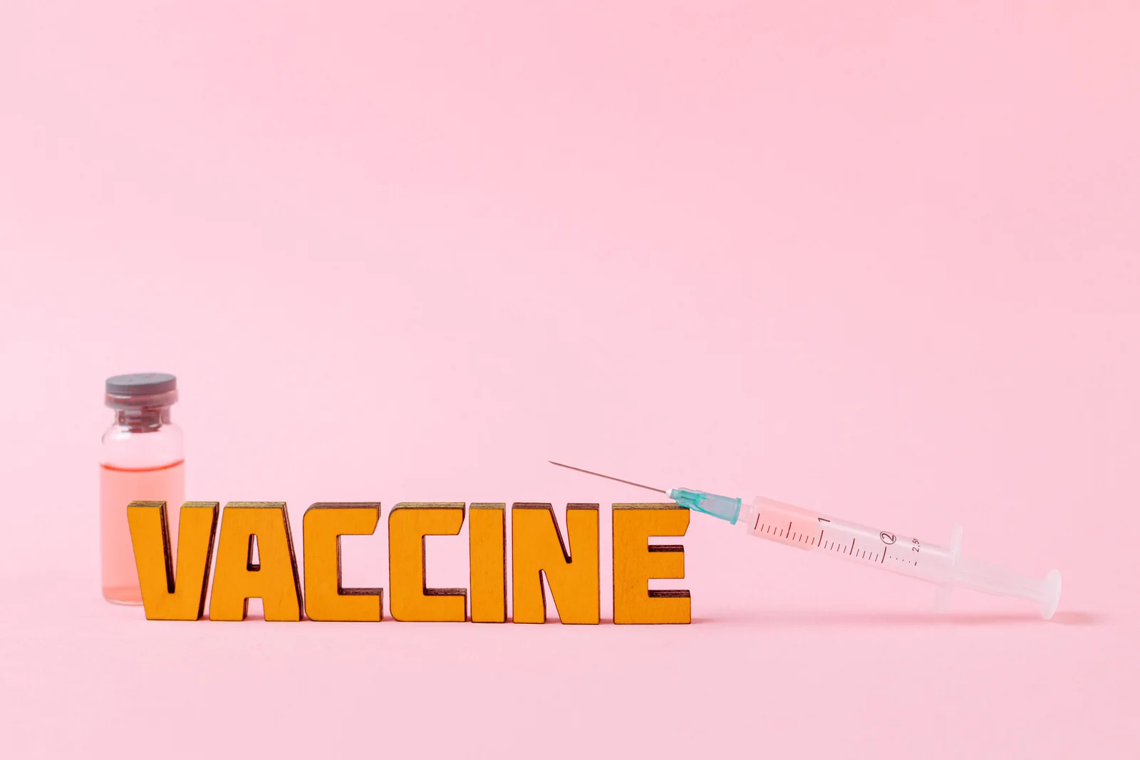 Close-up of a syringe and vaccine vial on a pink backdrop for health concepts.