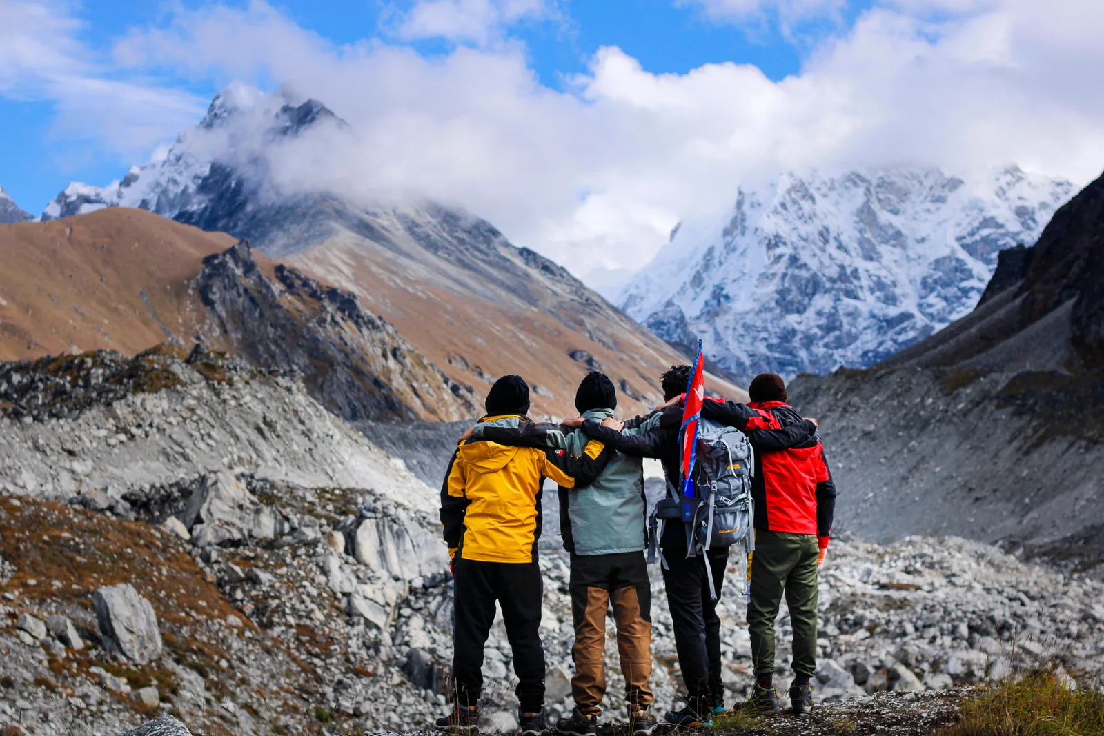 Four hikers stand arm in arm, embracing the majestic snowcapped mountain landscape.