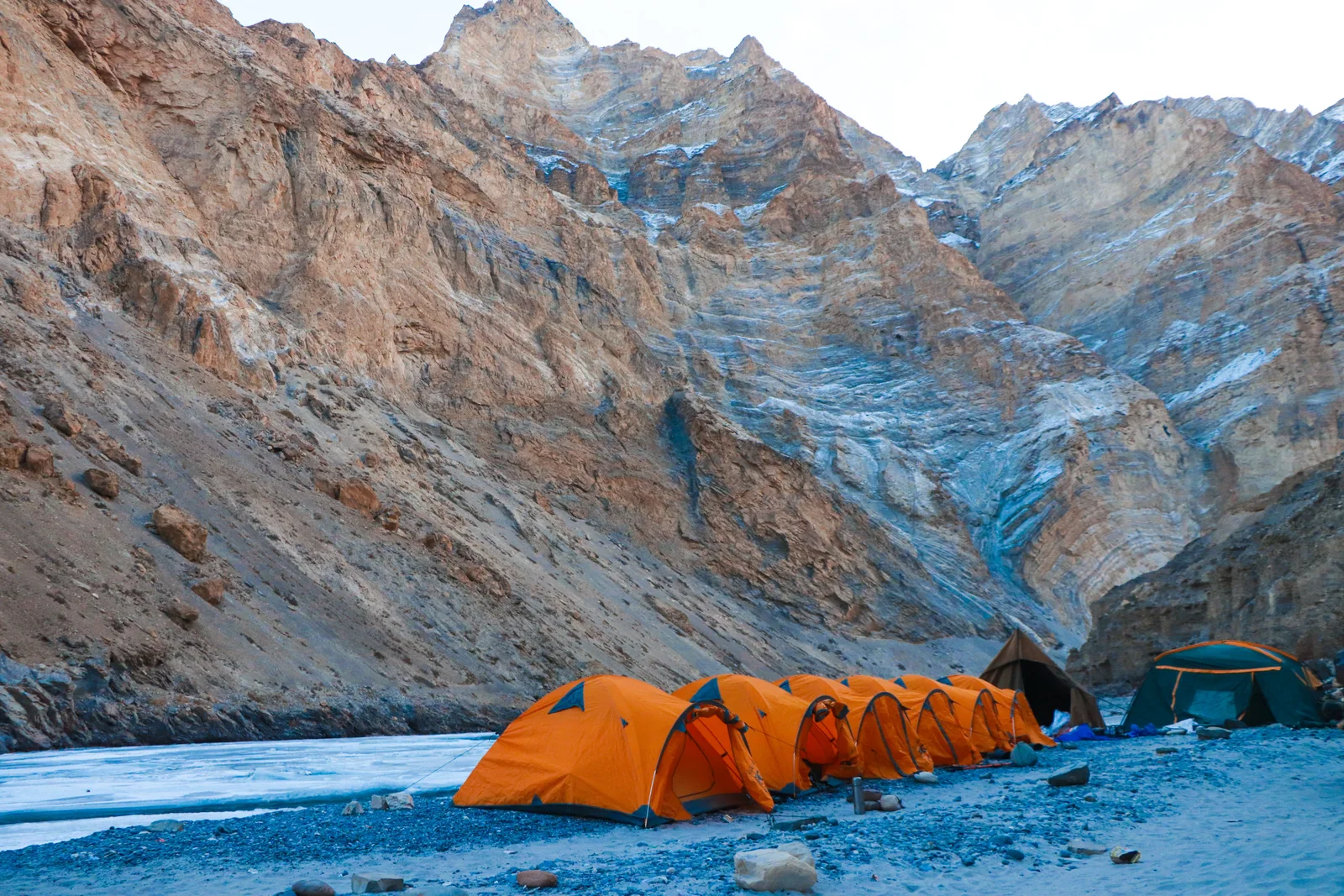 Orange tents pitched beside a frozen river in a mountain gorge